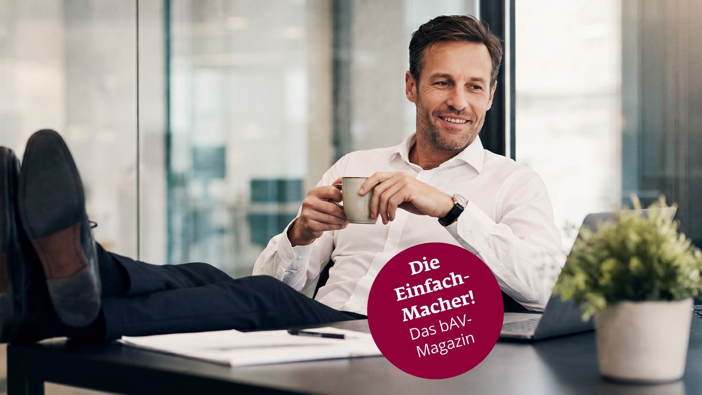 Ein lächelnder Mann sitzt am Schreibtisch und hat die Füße lässig auf dem Tisch liegen.