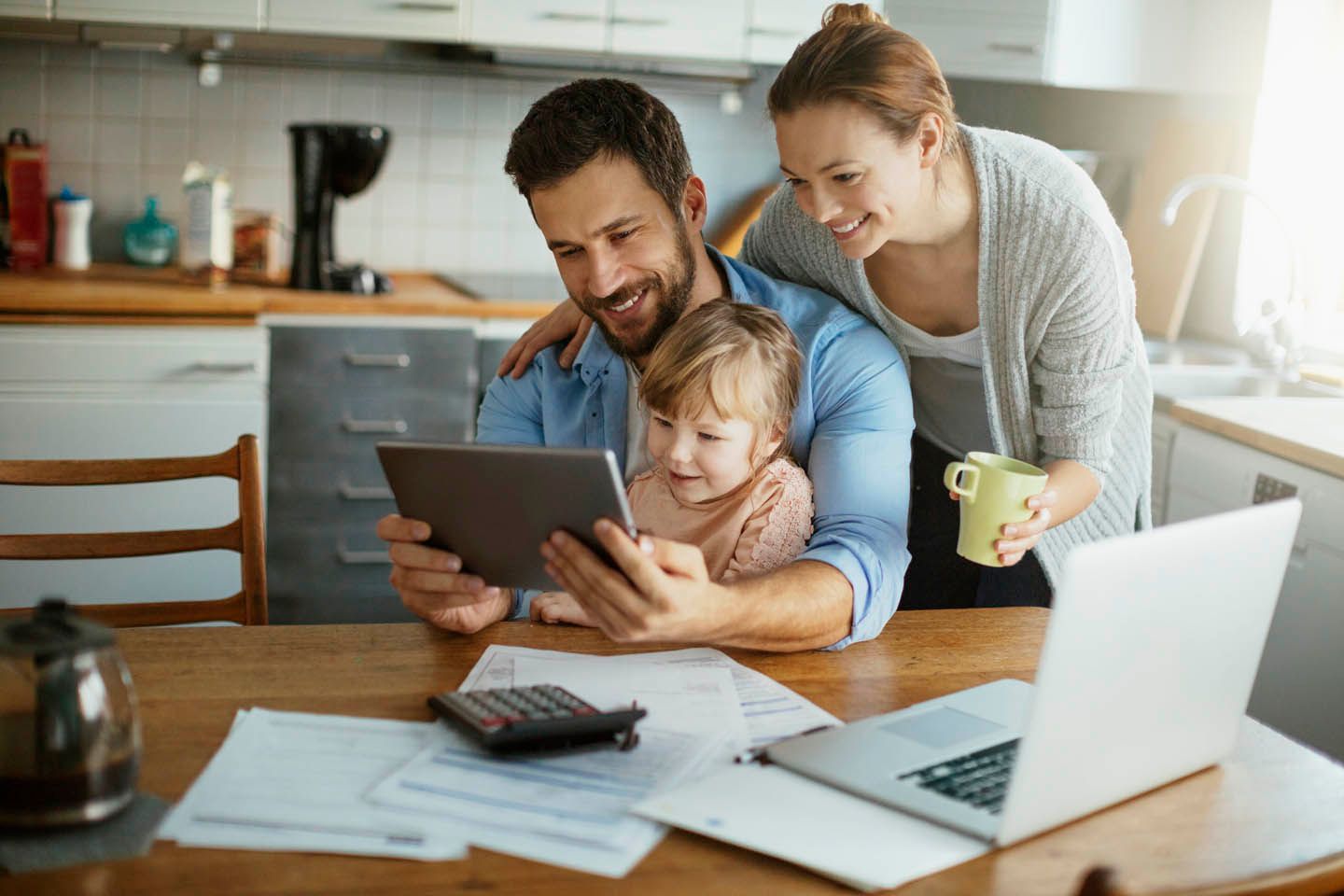 Vater sitz mit Tochter auf dem Schloß am Esstisch und schaut ins Tablet. Ehefrau schaut dabei über die Schulter.