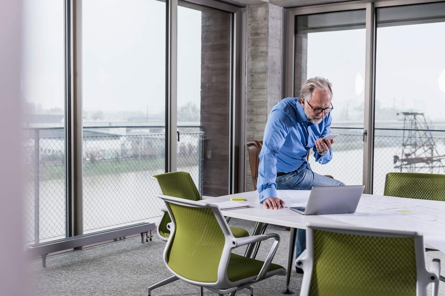 Älterer Geschäftsmann mit Smartphone und Laptop in einem Konferenzraum.