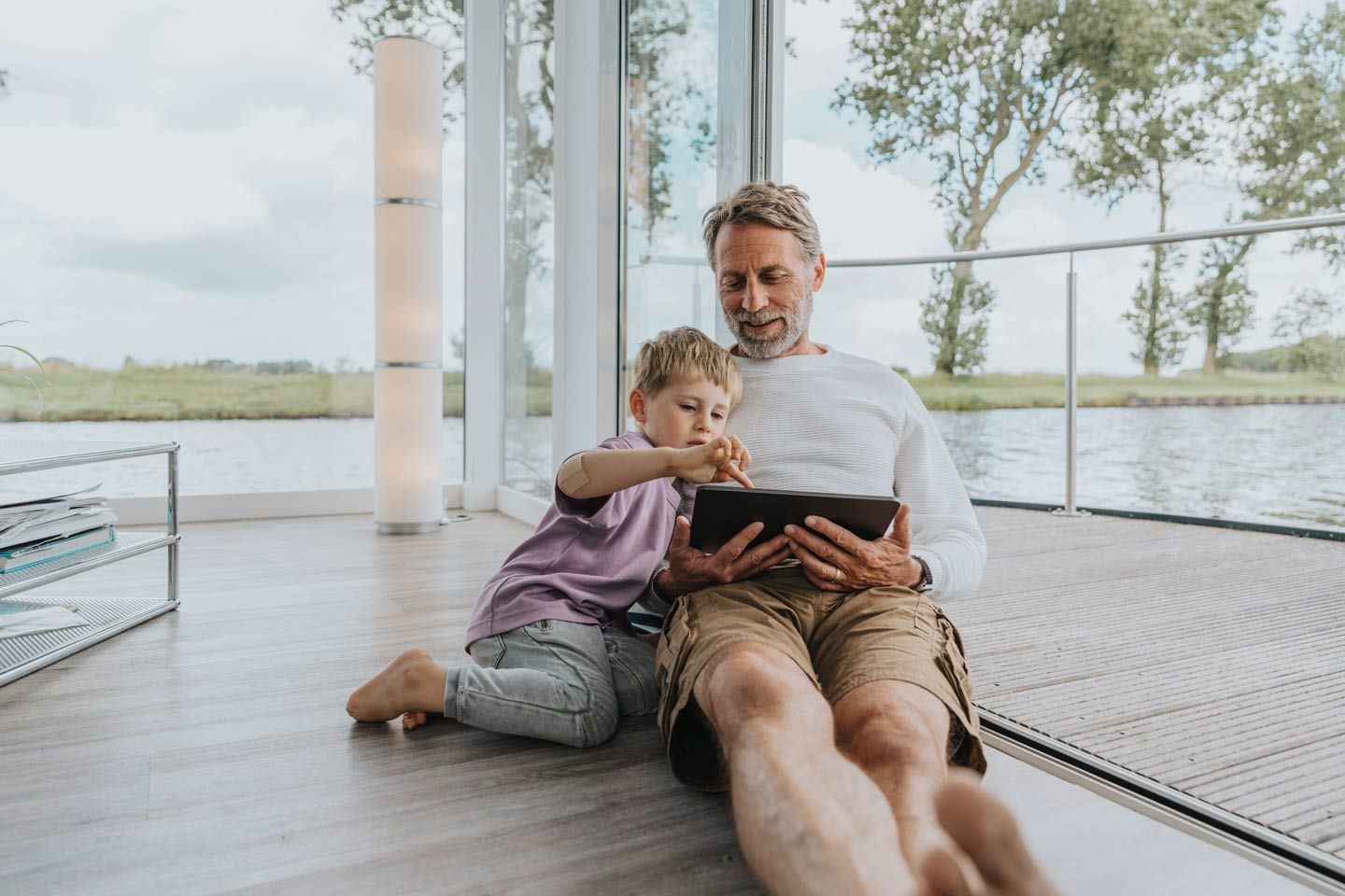 Vater und Sohn sitzen entspannt mit einem Tablet auf dem Boden.