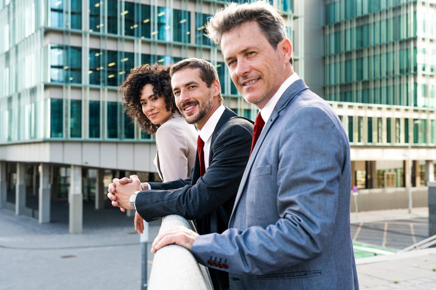 Drei Geschäftsleute stehen an einem Geländer und blicken zur Kamera.