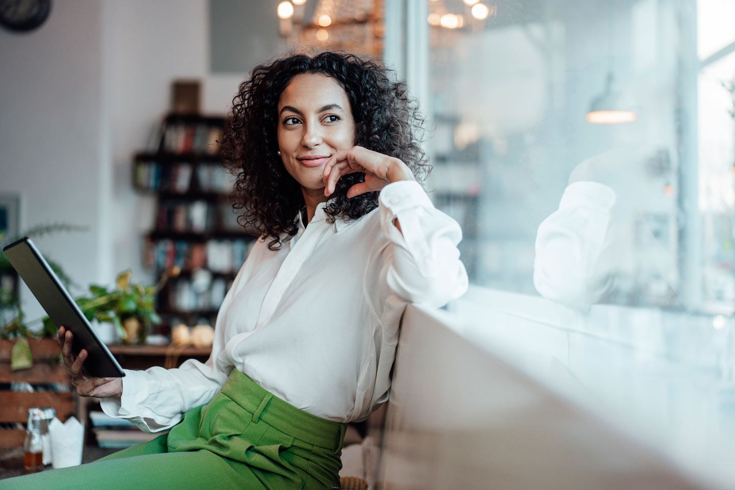 Eine Frau sitzt mit ihrem Tablet in einem Cafe.