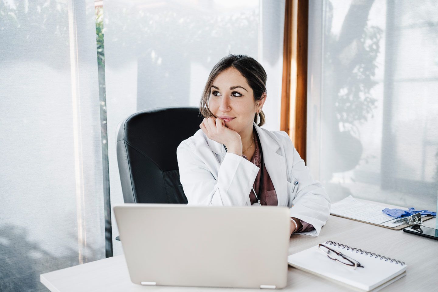 Weibliche medizinische Fachkraft sitzt verträumt am Schreibtisch.