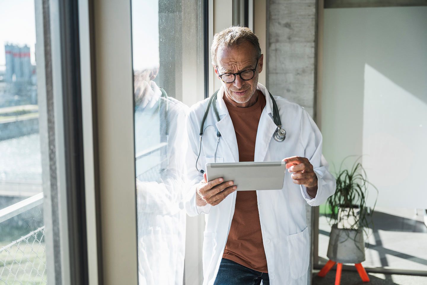Oberarzt mit Tablet steht am Fenster.