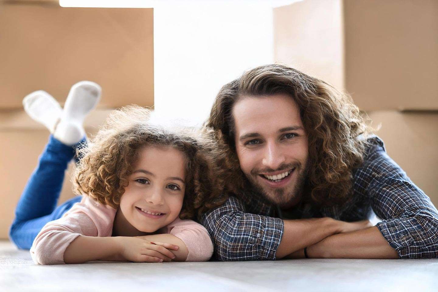 Ein Mann und ein Mädchen liegen nebeneinander auf dem Boden und lächeln fröhlich in die Kamera.