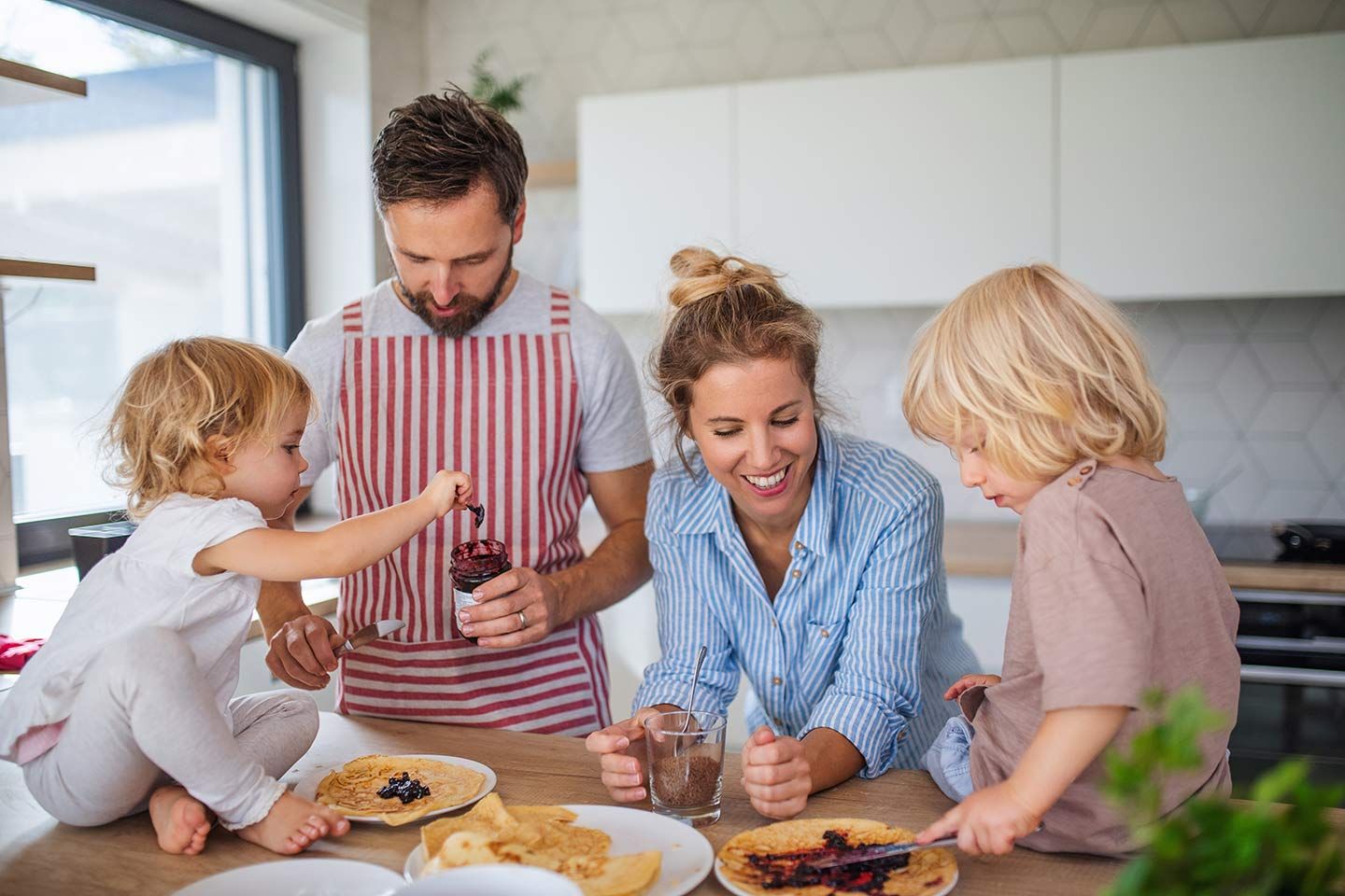 Junge Familie frühstückt gemeinsam in der Küche und bereiten Pfannkuchen mit Marmelade zu.