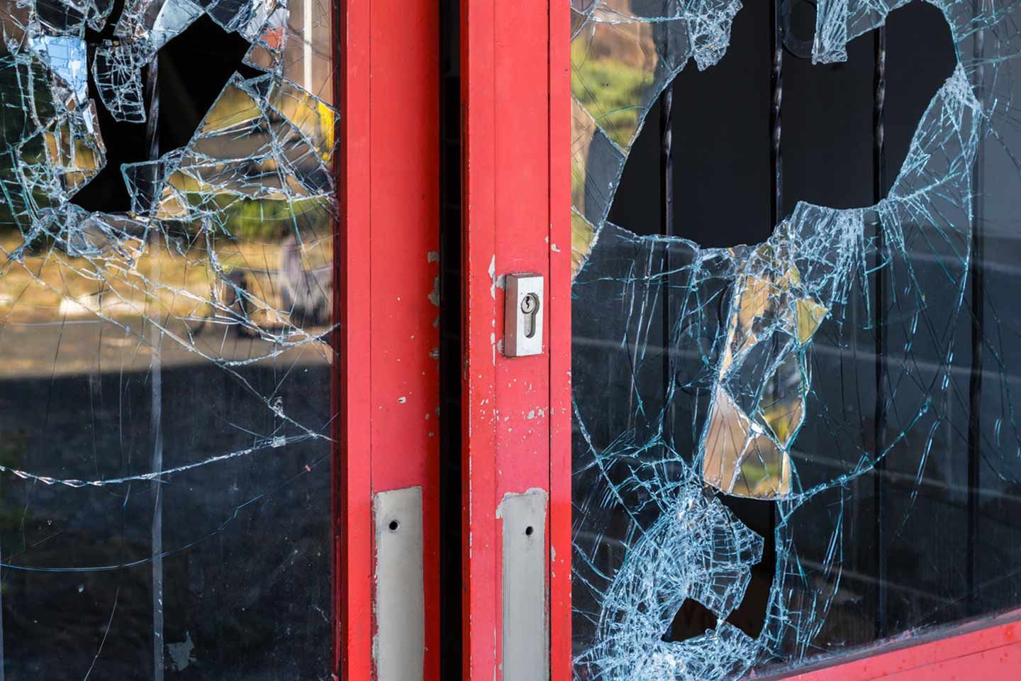 Zwei rote Glastüren mit großen, zersplitterten Scheiben und sichtbaren Einschlaglöchern.