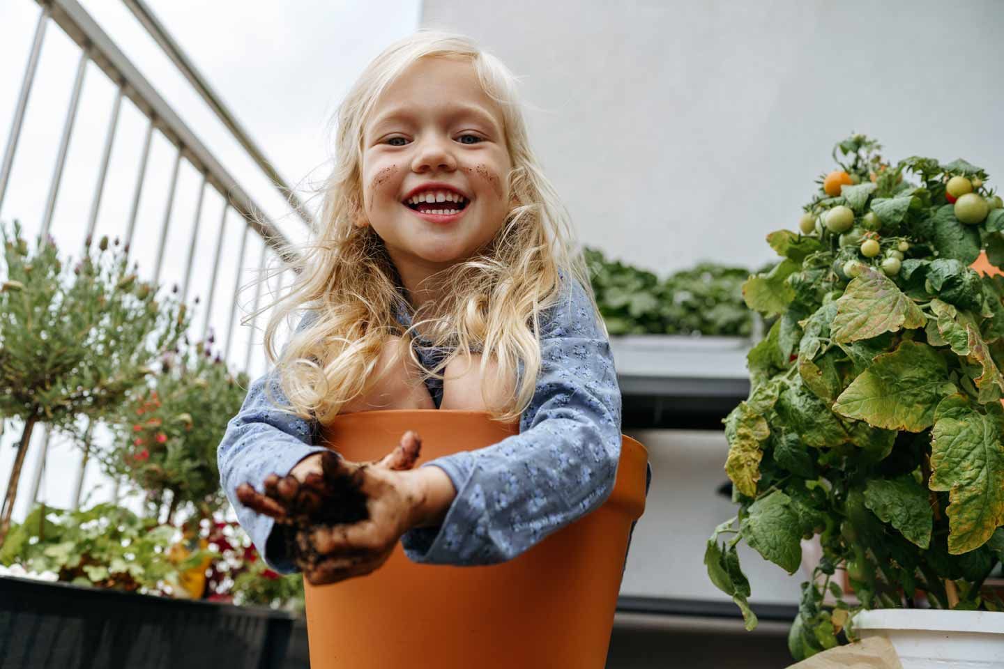 Lachendes Kind mit Erde an den Händen im Blumentopf.