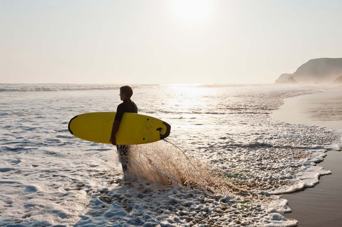 Junger Mann geht mit seinem Surfbrett ins Meer.