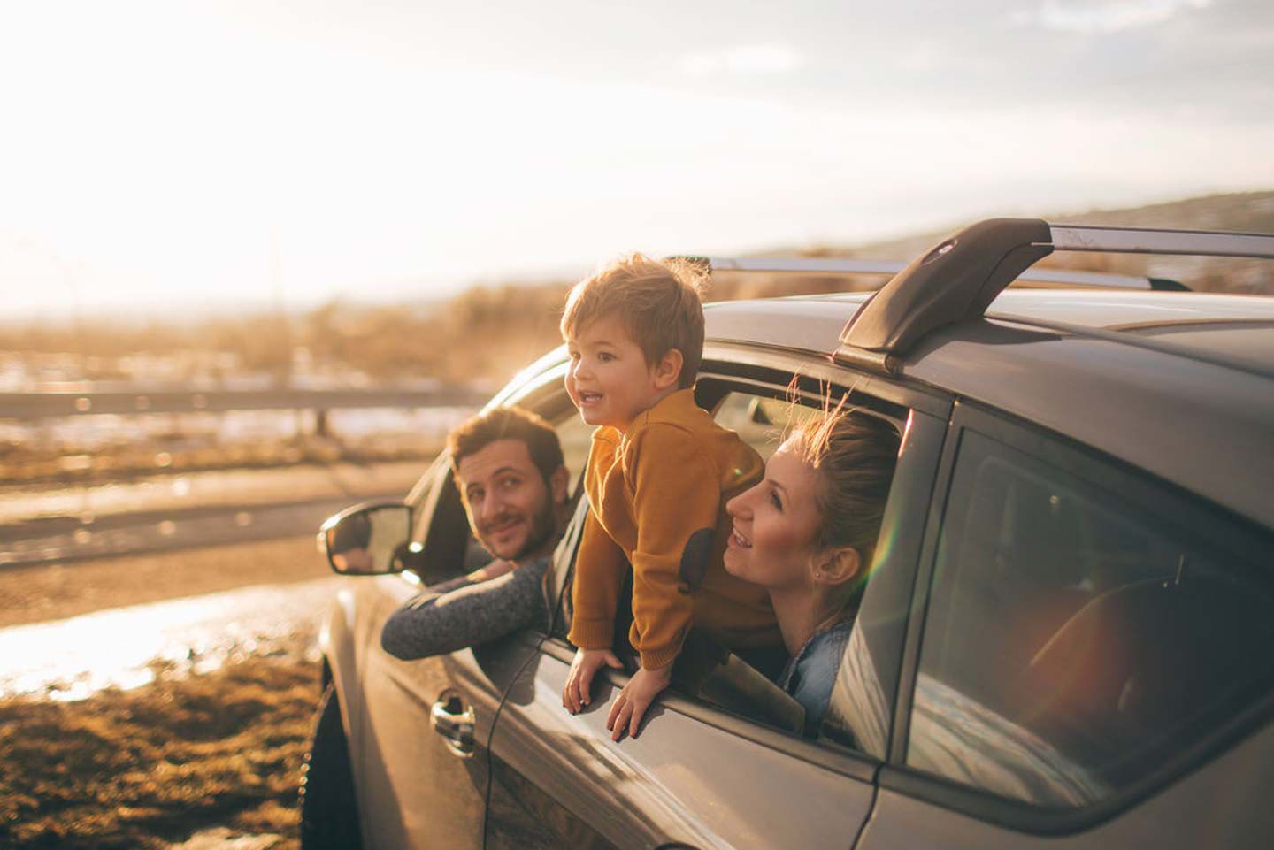Eine Familie schaut lachend aus dem Autofenster und genießt gemeinsam die Fahrt.