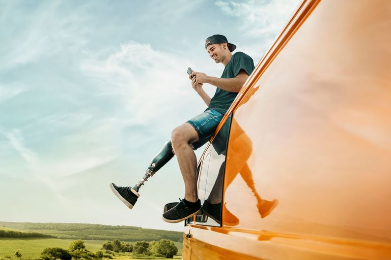 Mann mit Prothese sitzt am orangefarbenen Van vor Landschaft und Himmel.