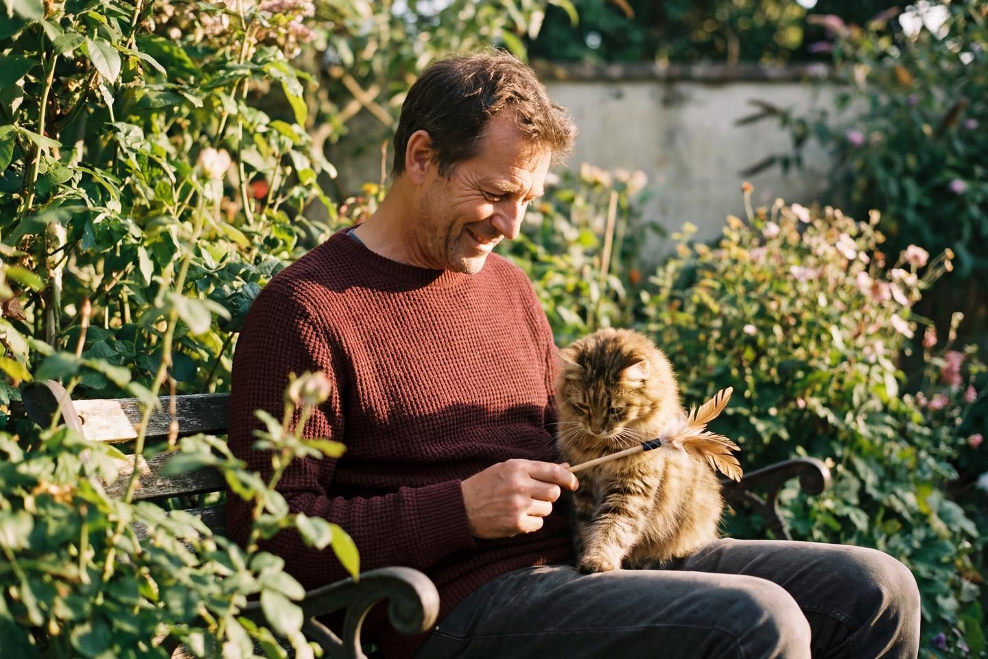 Ein Besitzer spielt mit seiner Katze im Garten auf einer Bank.