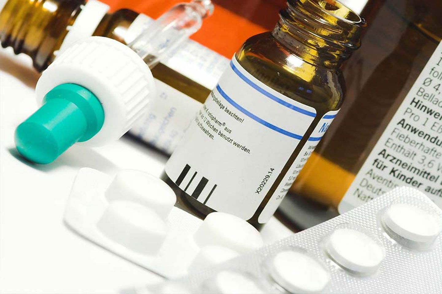 Verschiedene Medizinfläschchen und Tabletten liegen dicht beieinander auf einer weißen Unterlage.
