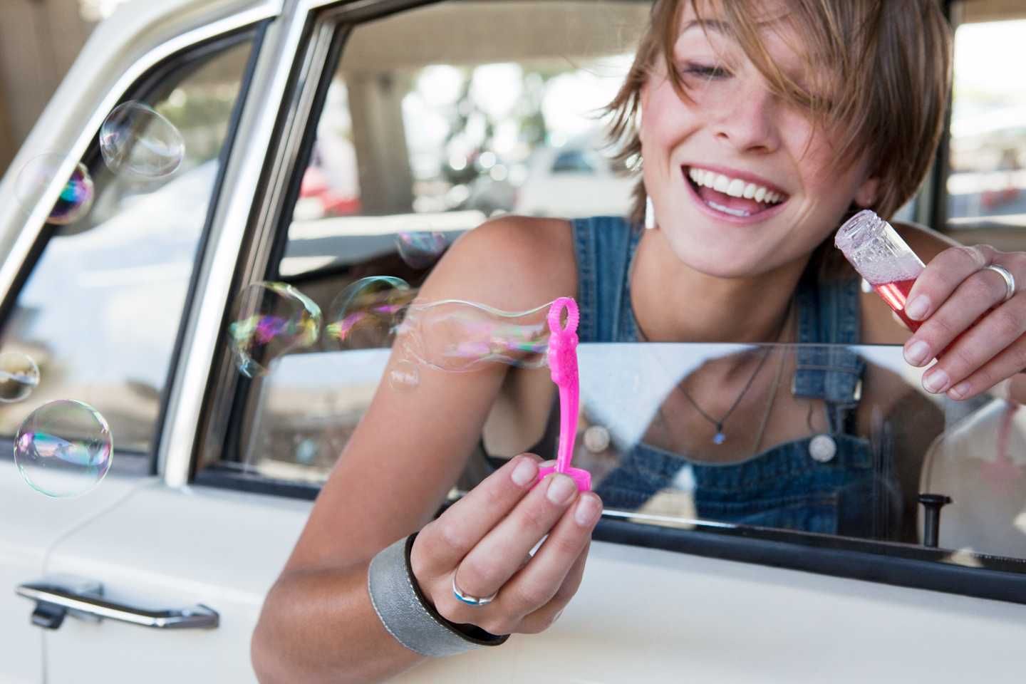 Eine junge Frau lehnt sich aus dem Autofenster und bläst Seifenblasen hinaus.