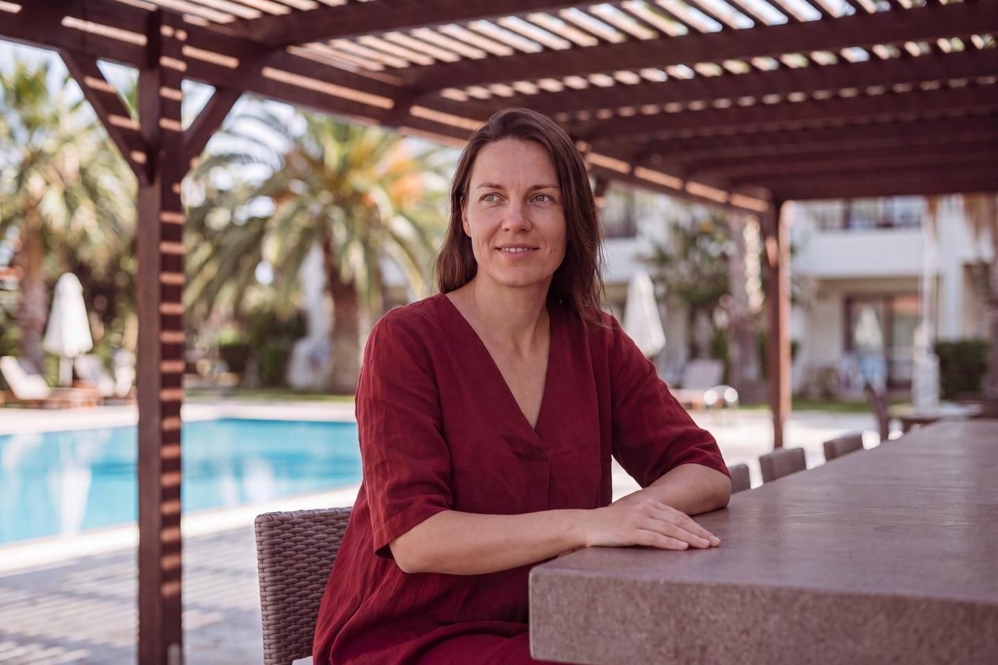 Frau sitzt an einer Theke, im Hintergrund eine Poollandschaft mit Palmen. (Bild KI-unterstützt generiert)