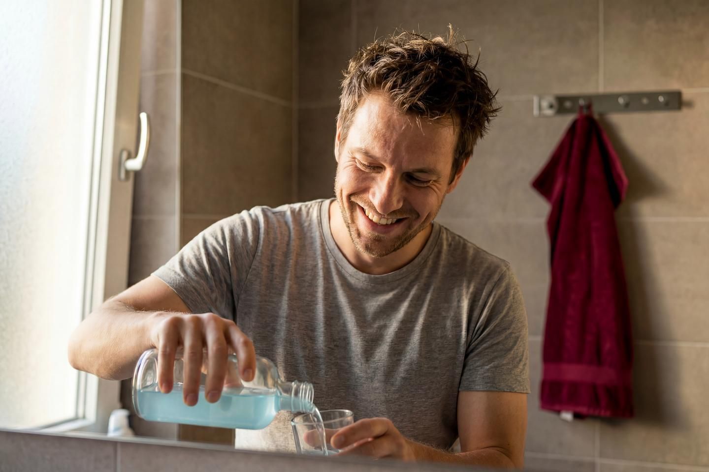 Lächelnder Mann füllt Mundspülung in ein Glas.