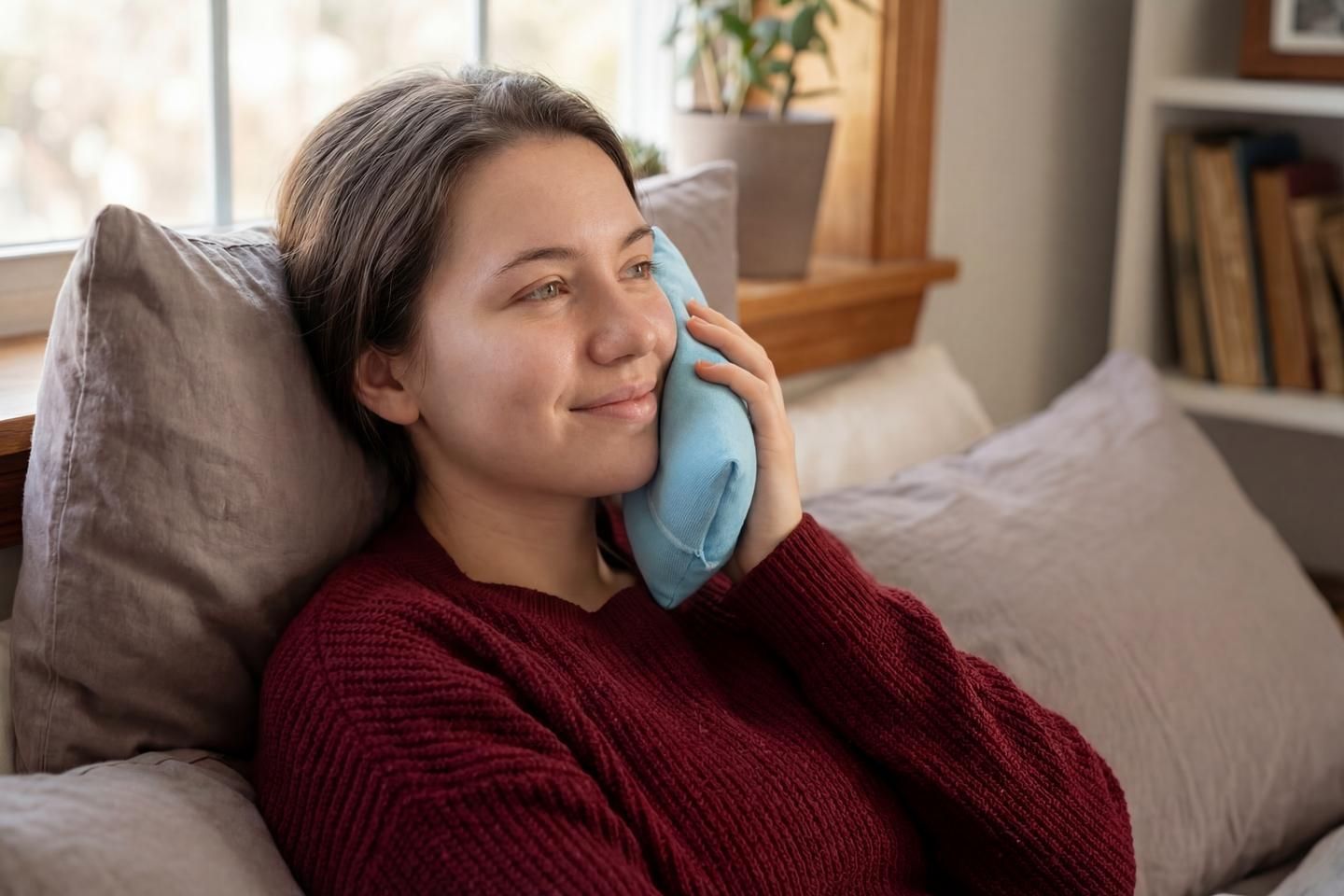Eine Frau kühlt ihre Backe auf dem Sofa.