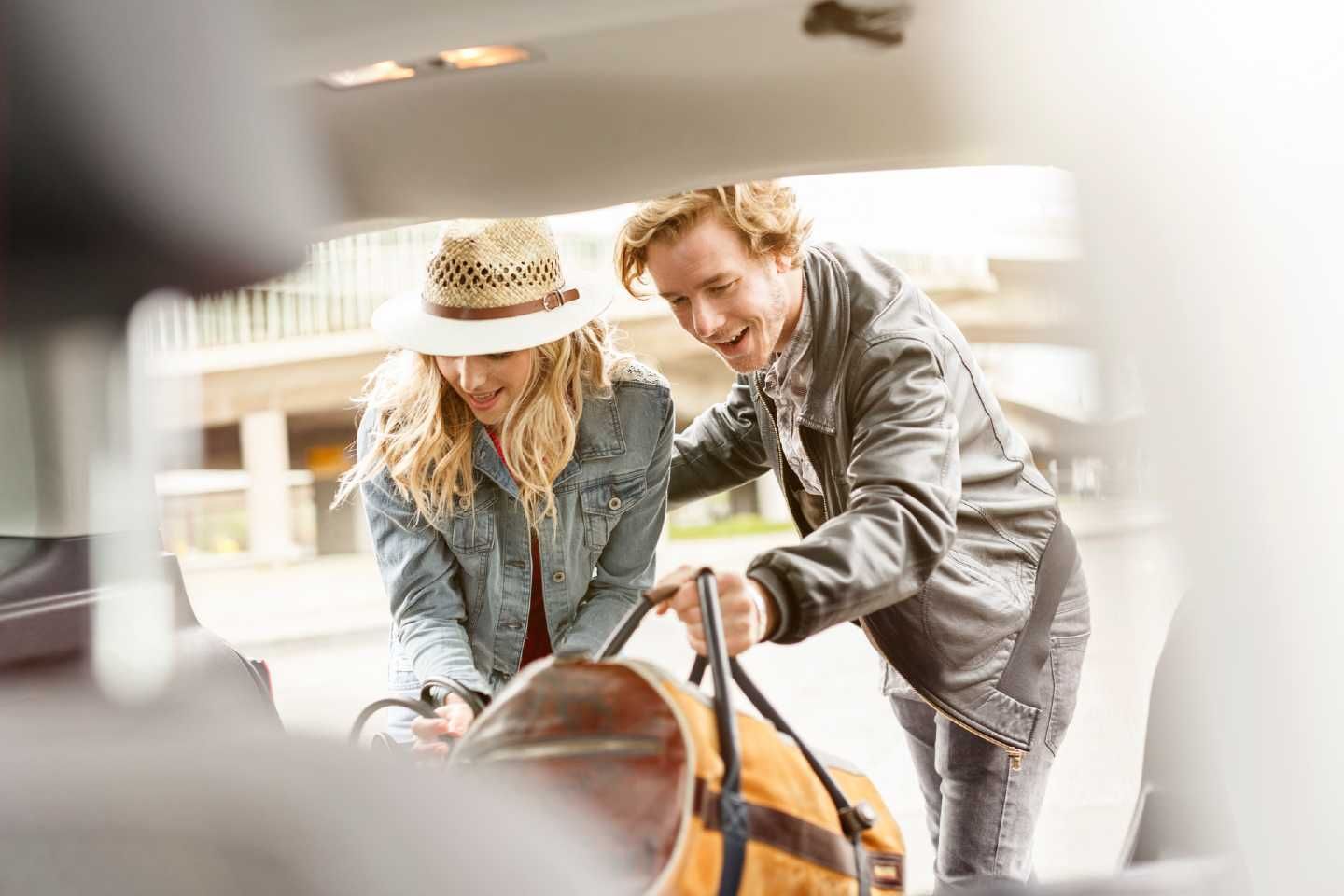 Pärchen legt Gepäck in den Kofferraum ihres Autos.