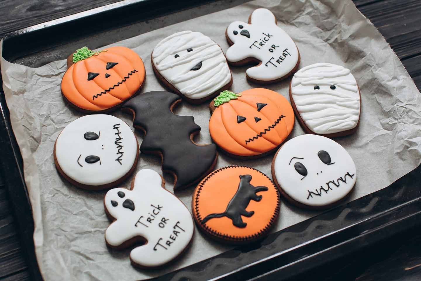Kekse in Form von Geistern und Kürbissen, für Halloween dekoriert auf einem Backblech. 