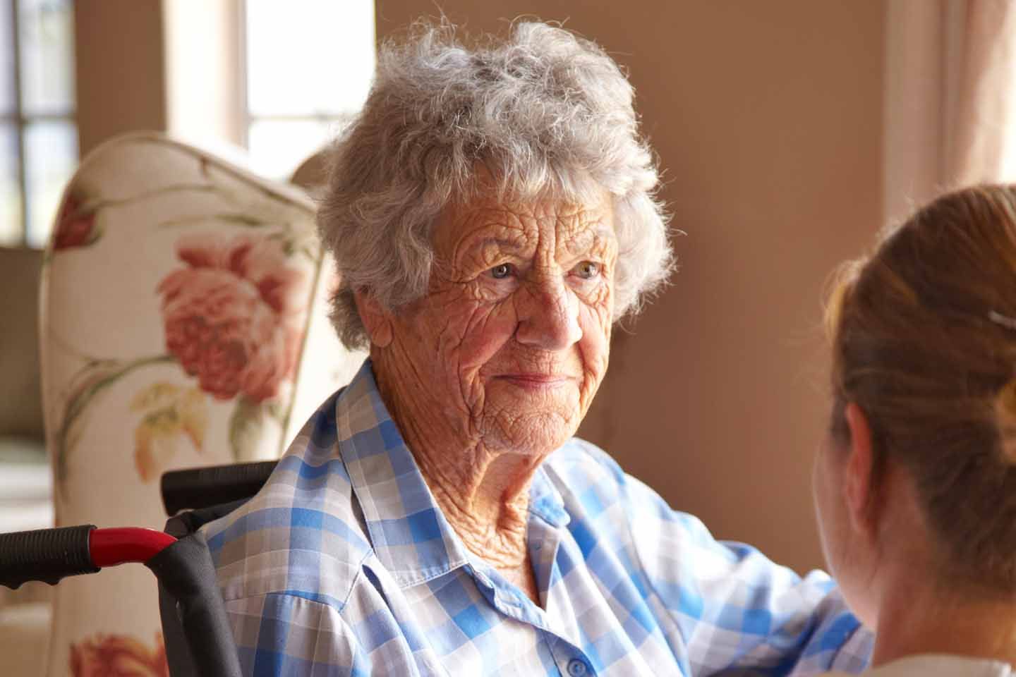 Eine ältere Frau im Rollstuhl unterhält sich mit der Pflegerin.