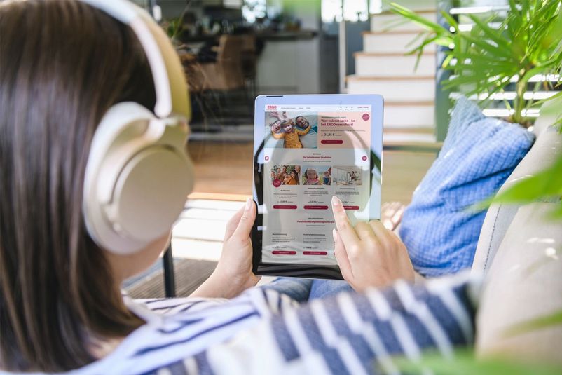 Frau mit Kopfhörer sitzt auf dem Sofa und arbeitet am Tablet