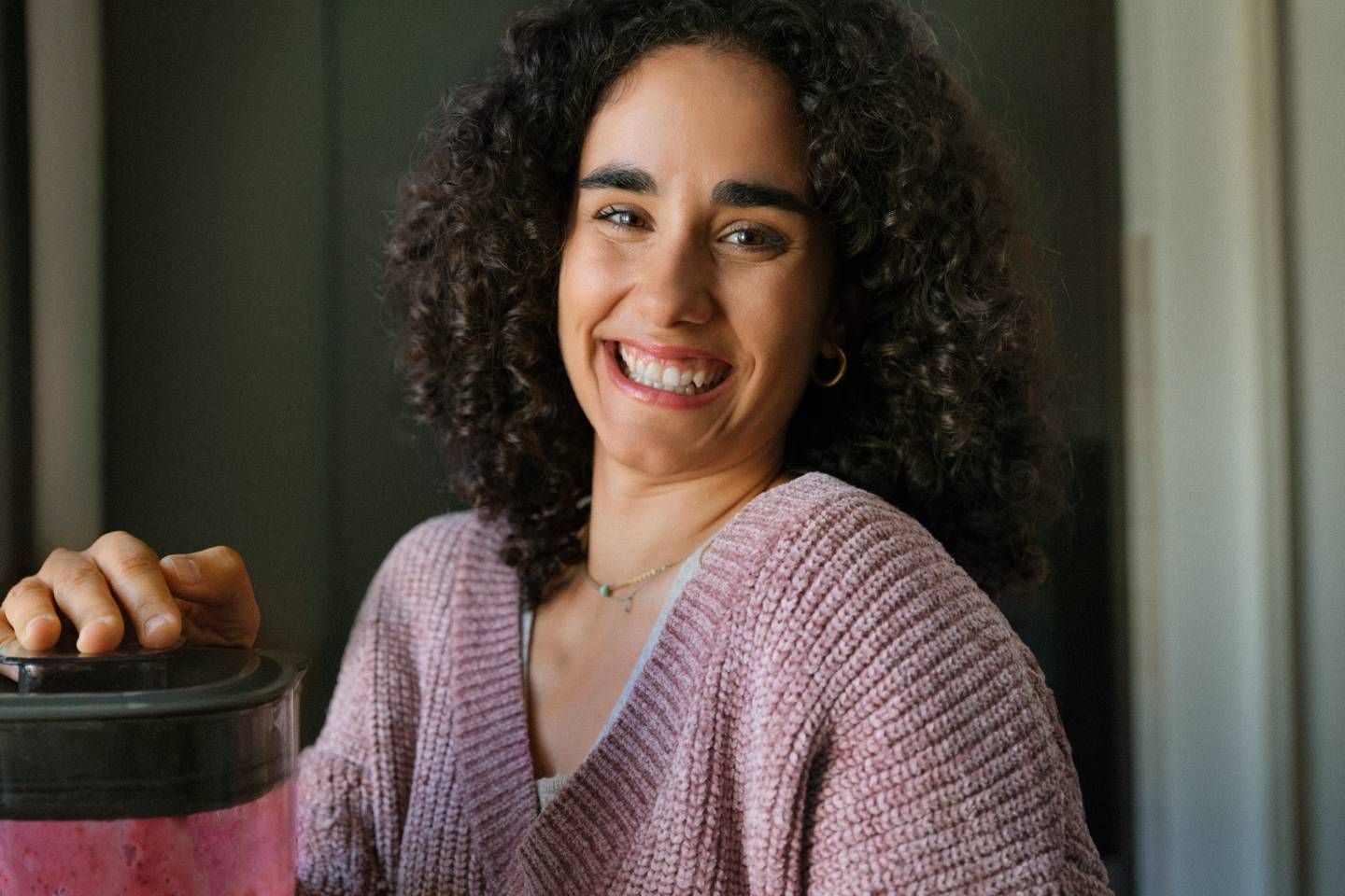 Lächelnde Frau mit lockigen Haaren hält einen Mixerbehälter in der Hand