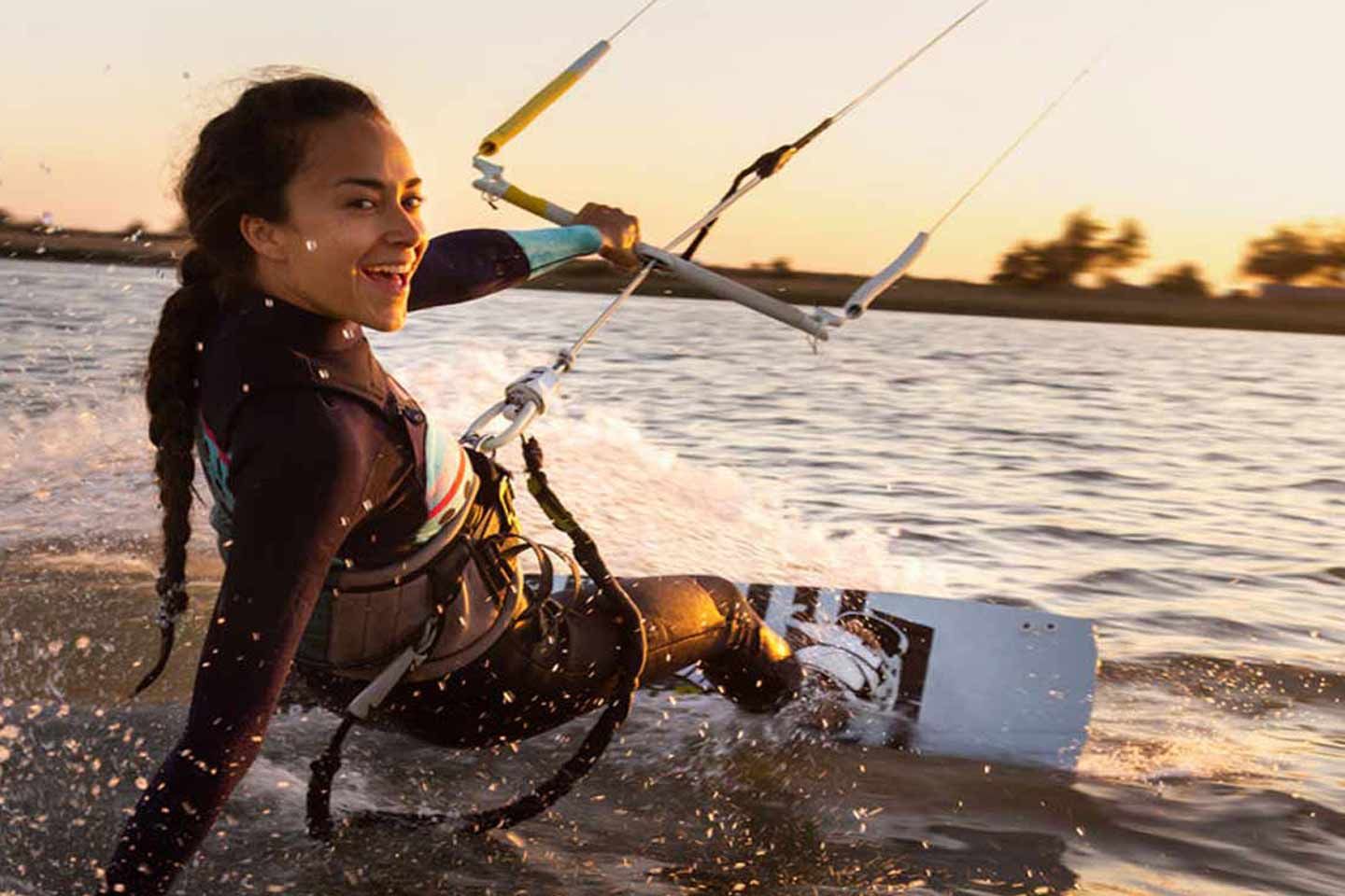 Frau beim Kitesurfen bei Sonnenuntergang.