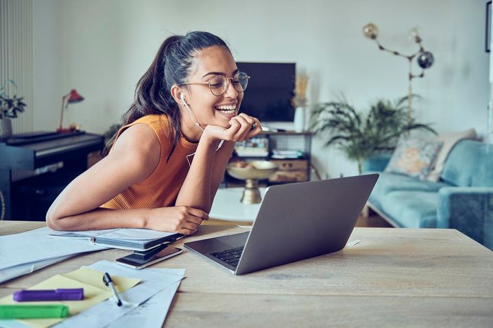 Junge Frau mit Headset sitzt lachend an ihrem Laptop.