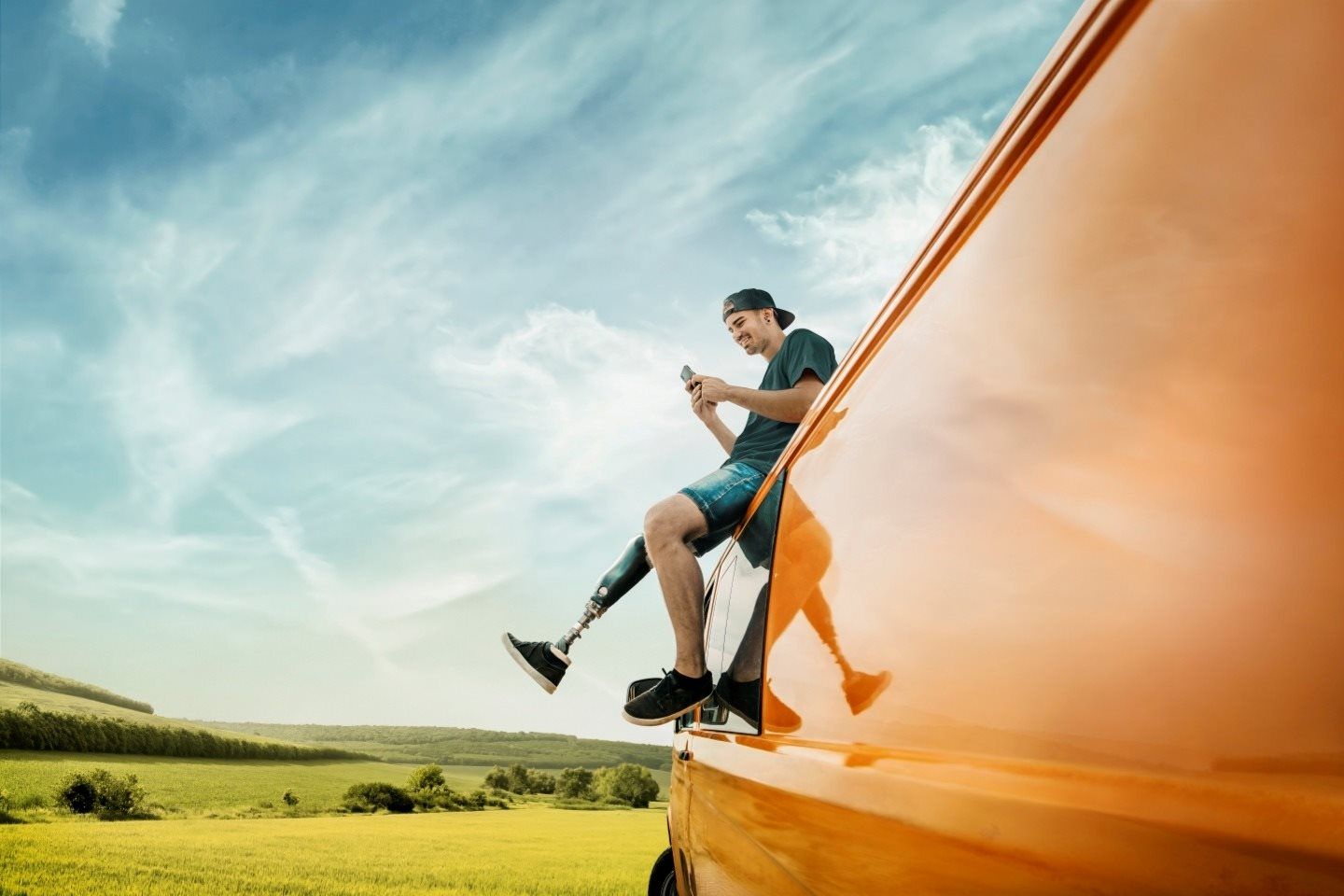 Junger Mann sitzt auf dem Autodach und schaut in das Handy.