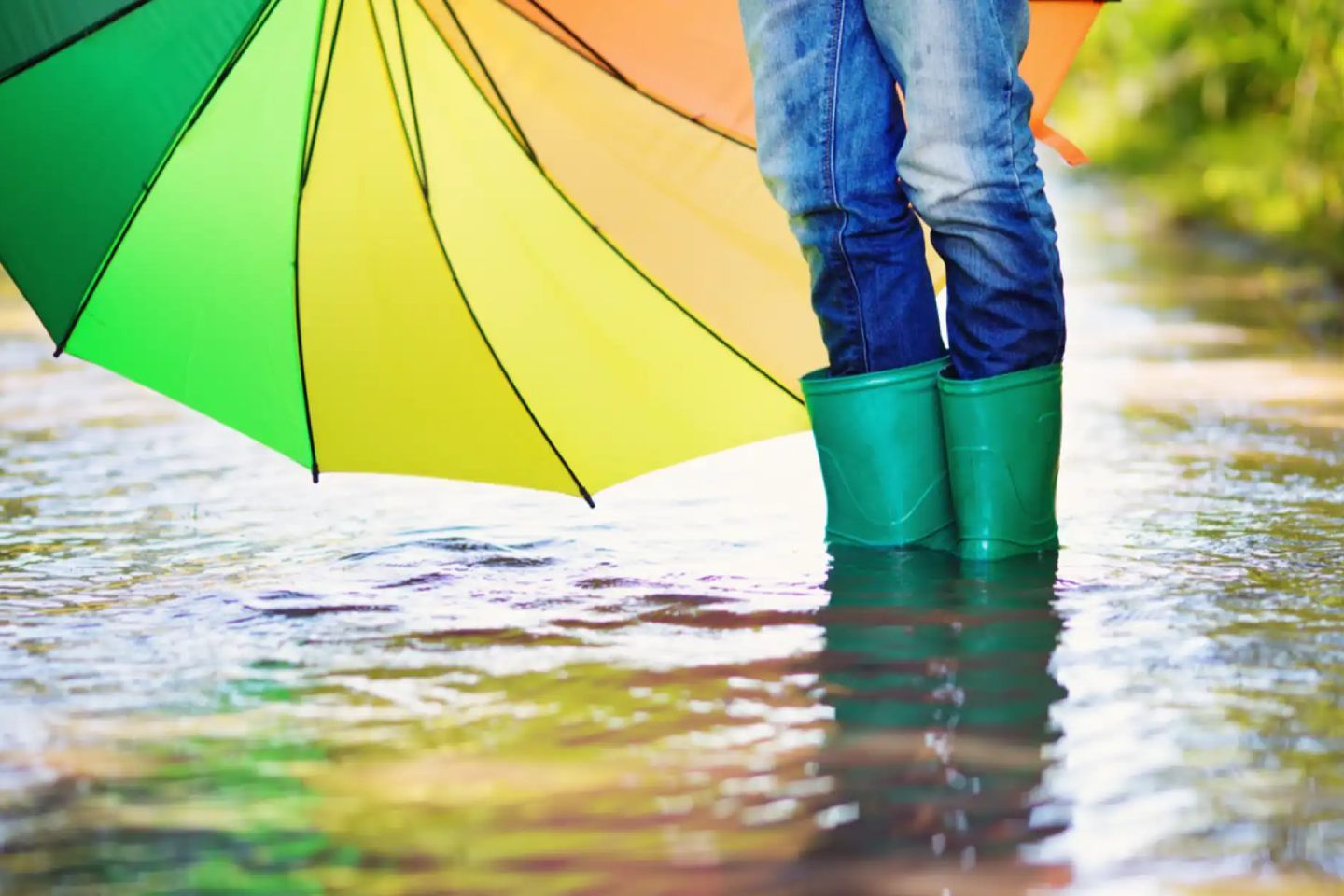 Eine Frau steht mit Regenschirm und Gummistiefeln im Hochwasser.