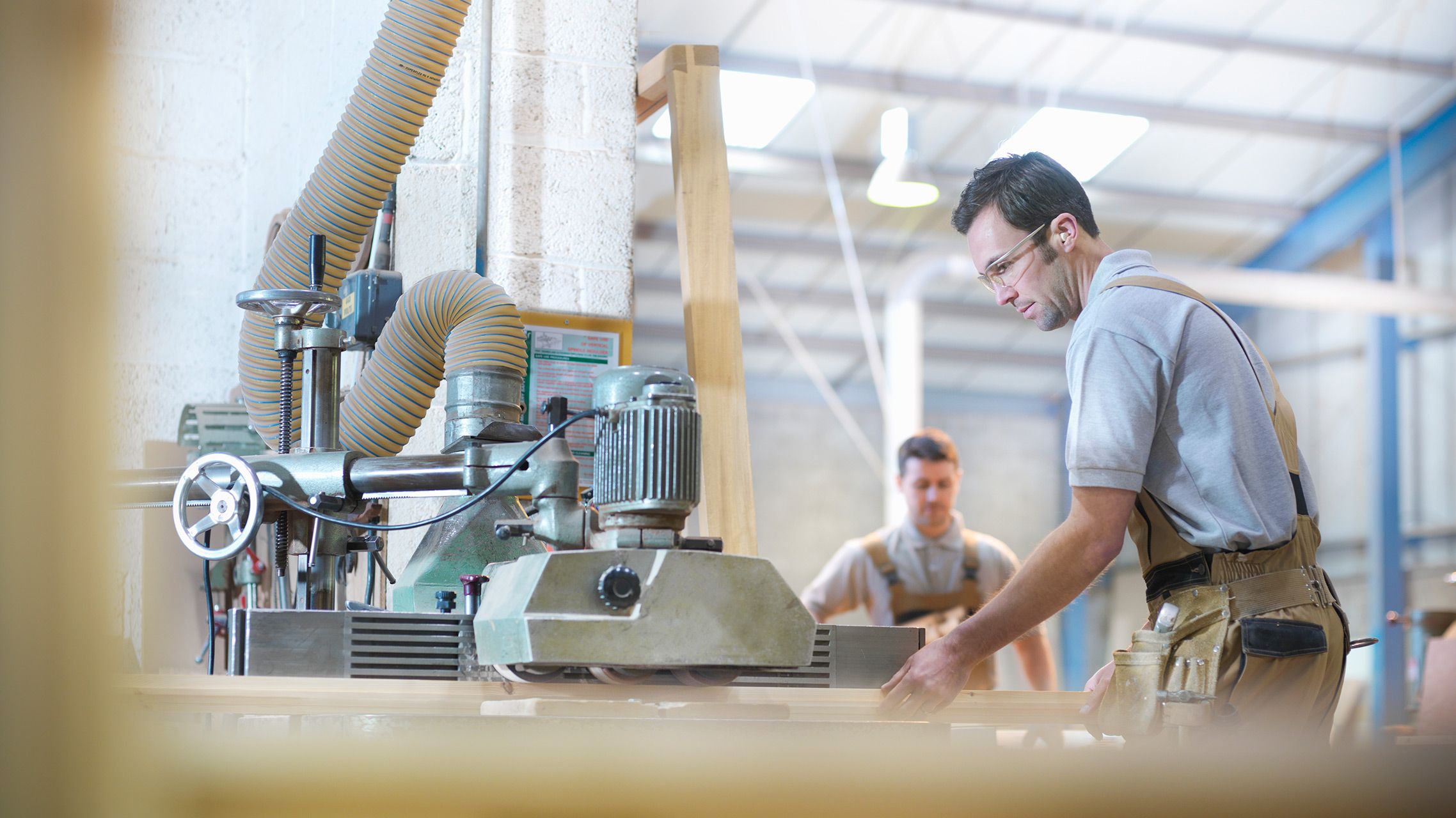 Schreiner mit Schutzbrille arbeitet an einer Holzbearbeitungsmaschine in einer Werkstatt.