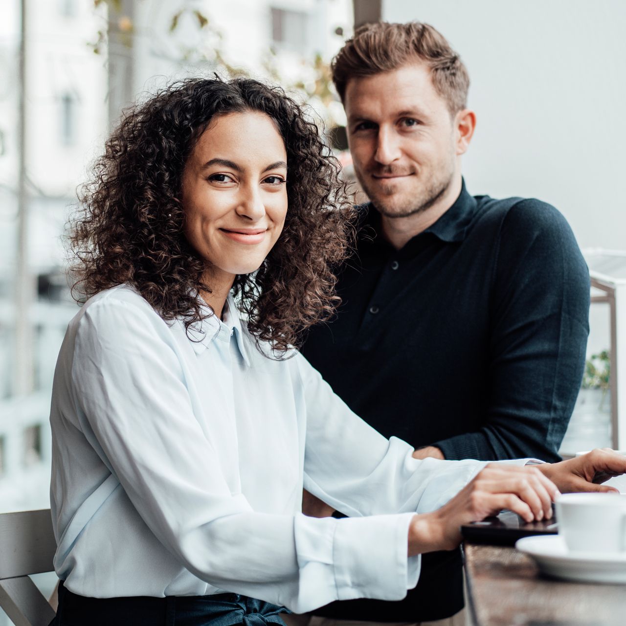 Frau und Mann in Businesskleidung vor einem Laptop mit einer Tasse Kaffee