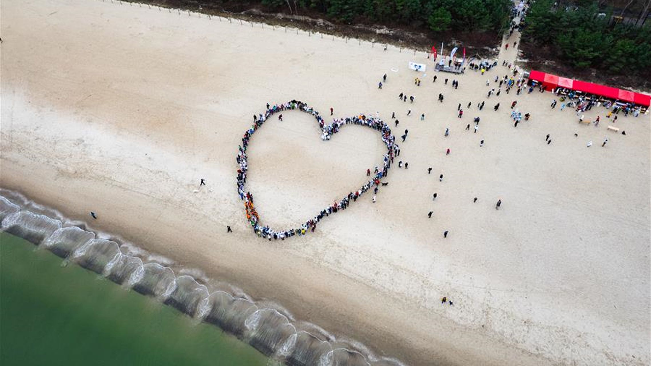 Personen formen ein Herz am Strand