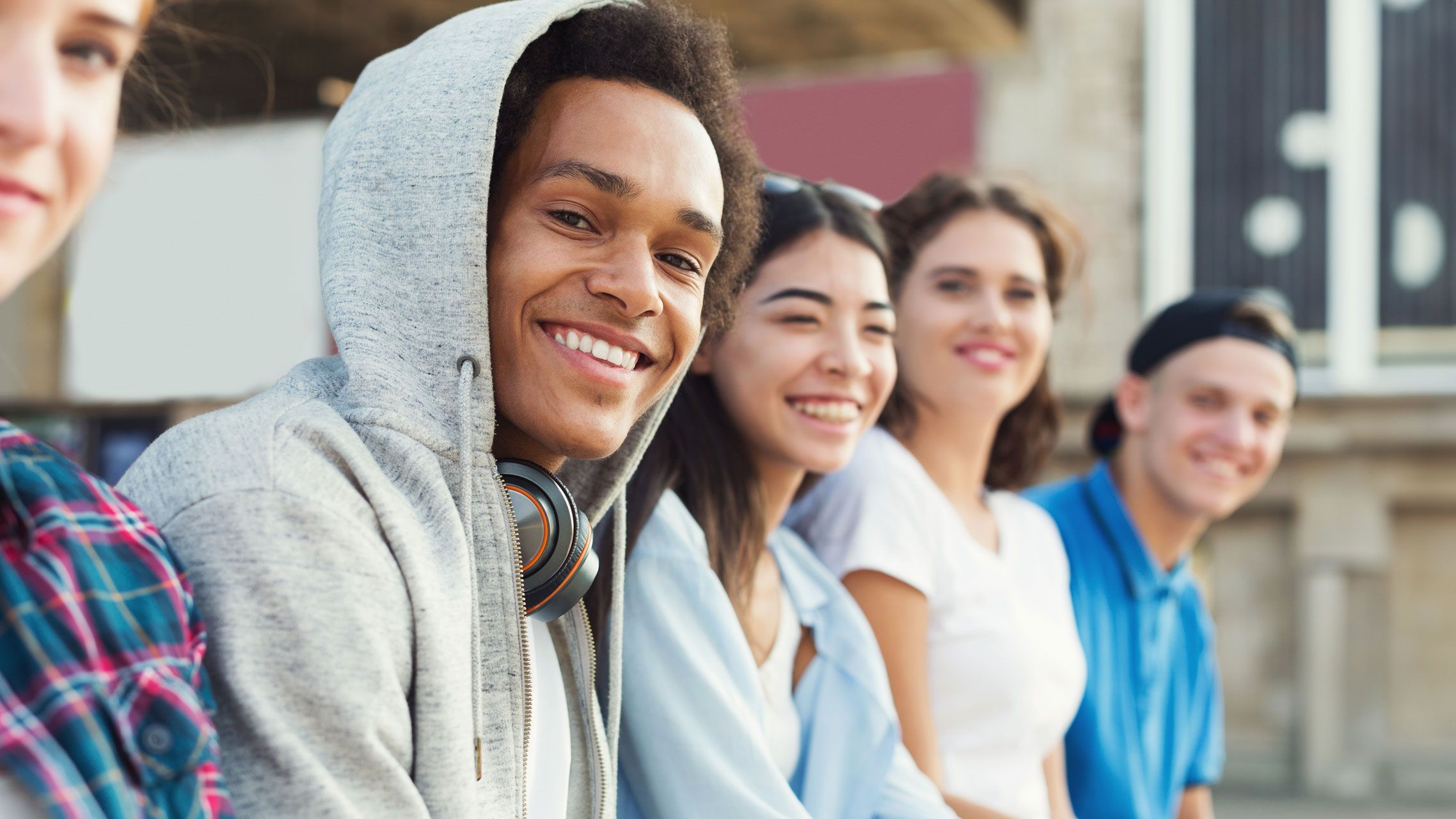 Jugendliche sitzen draußen und lachen in die Kamera.