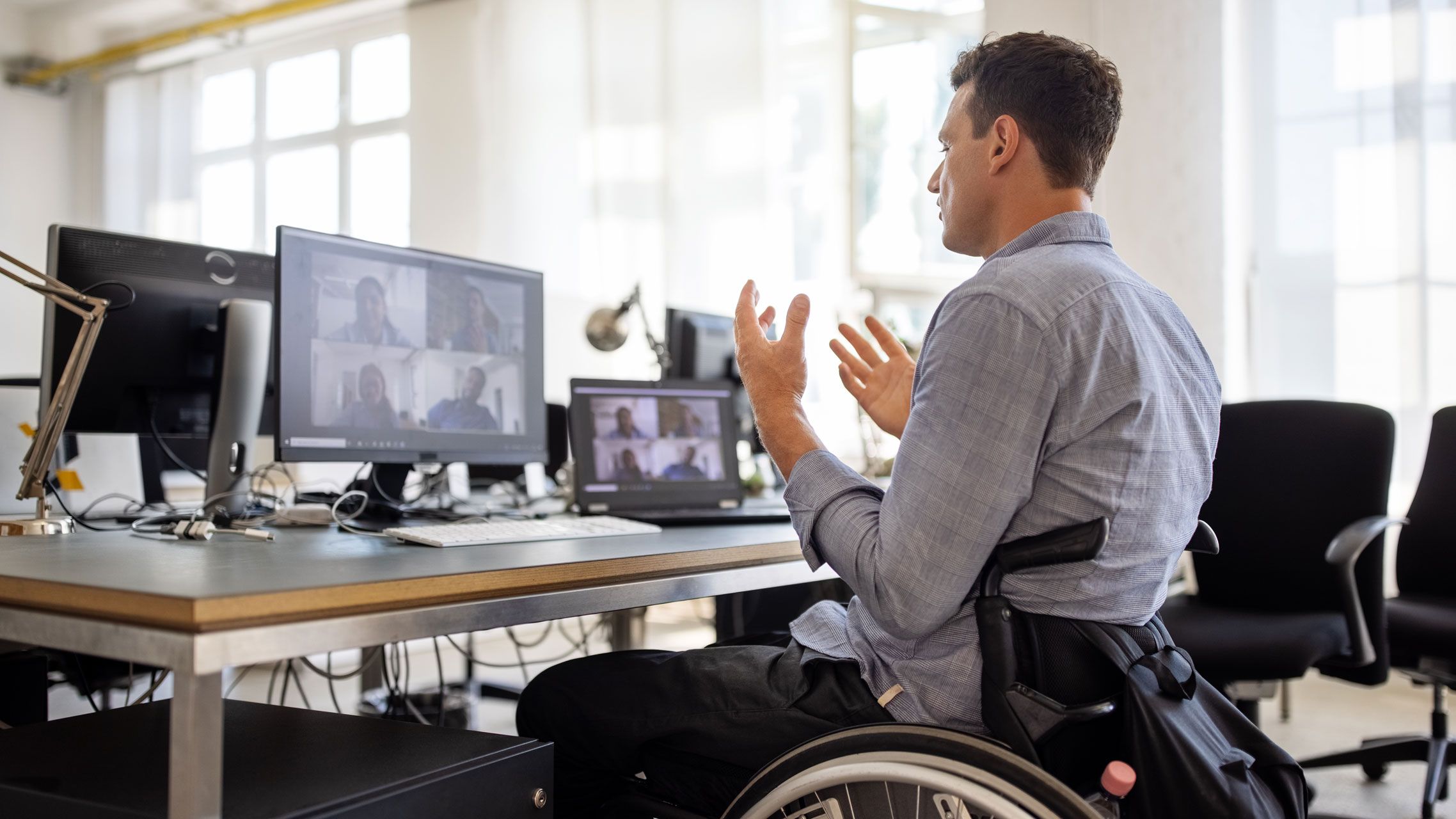 Ein Mann im Rollstuhl vor einem Schreibtisch in einer Videokonferenz.