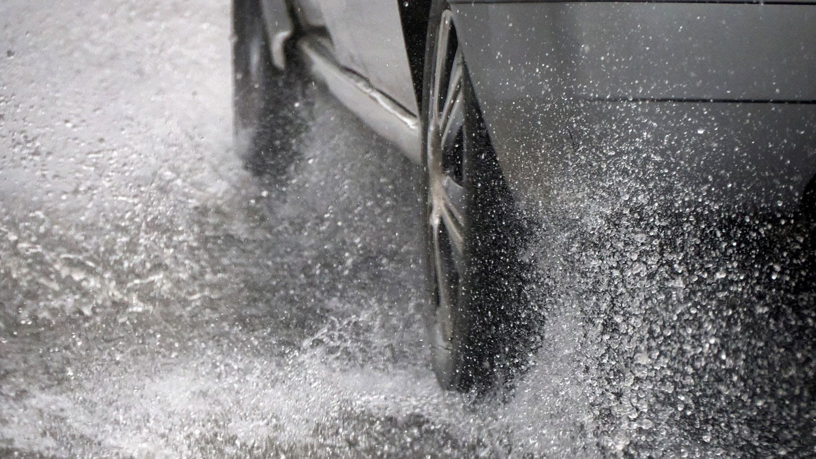 Ein Auto durchquert eine nasse Straße, die mit Wasser bedeckt ist.
