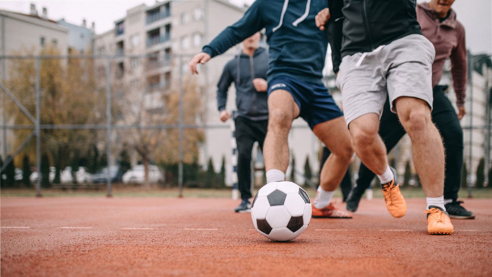 Vier Männer spielen Fußball und sind auf den Ball fokussiert.