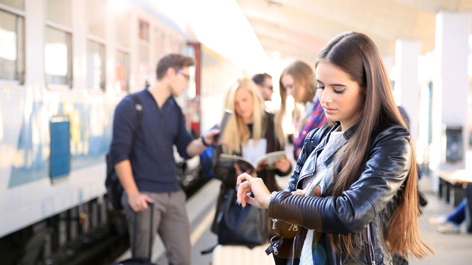 Eine Frau steht am Bahnsteig neben einem Zug und schaut auf ihre Armbanduhr.