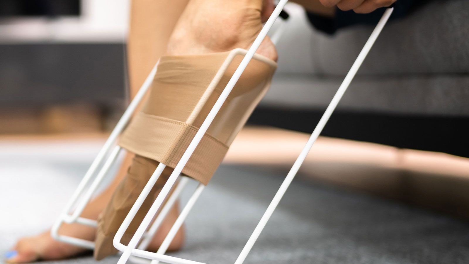 Eine Frau sitzt auf einem Sofa, einer ihrer Füße liegt auf einem Fußstützgerät.