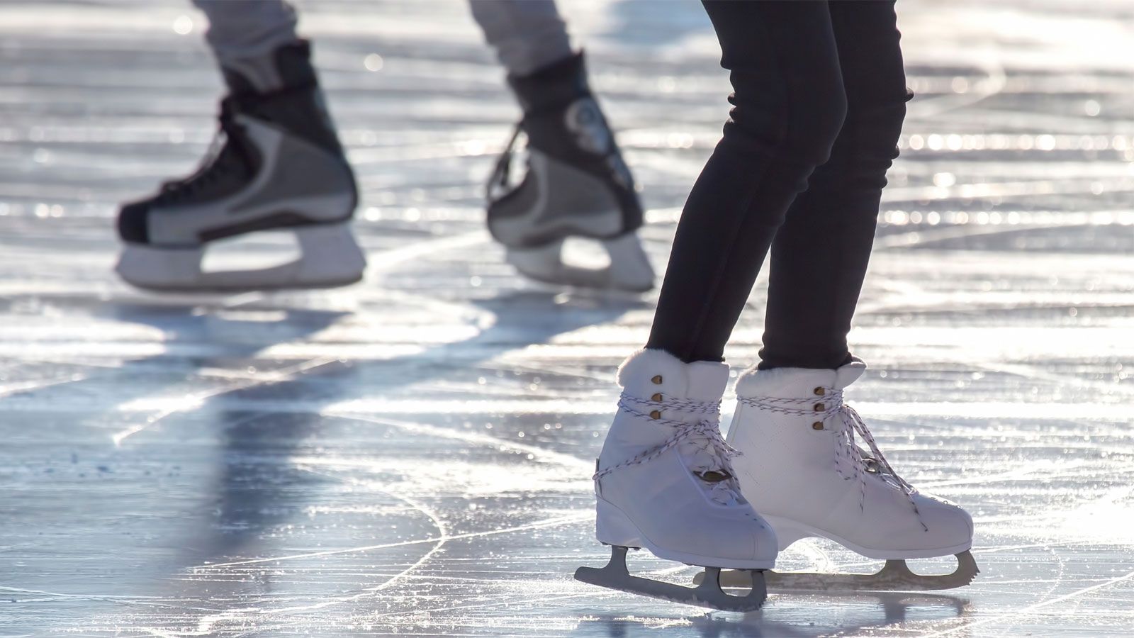 Auf einer Eisbahn stehen zwei Personen in Schlittschuhen.