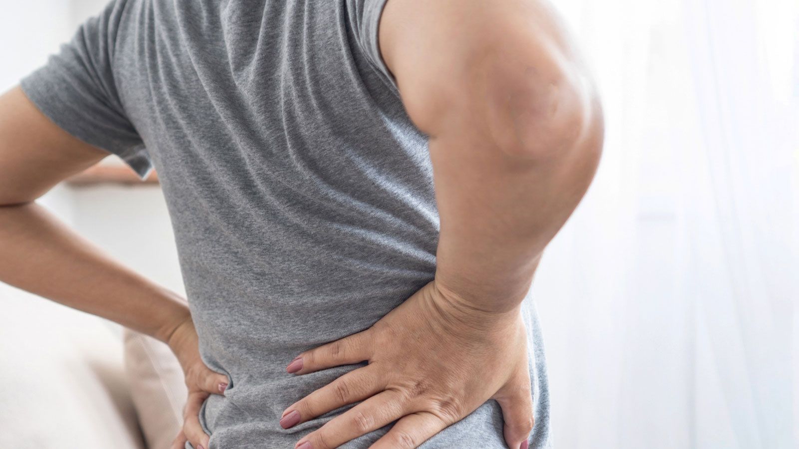 Eine Frau sitzt auf der Couch und hält sich den Rücken.