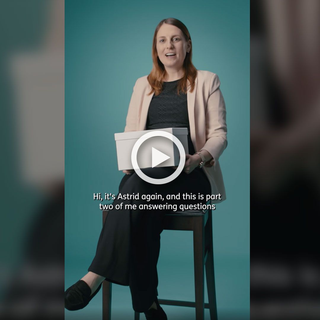 A woman sits on a stool in front of a blue screen with a white box on her lap.