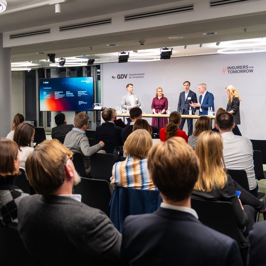Five people are chatting on a stage in front of a seated audience.