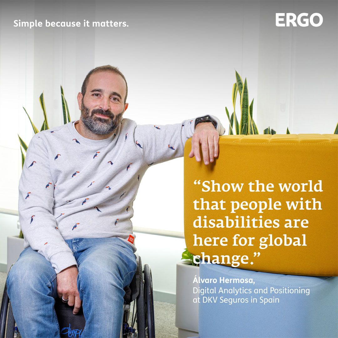 A man in a wheelchair poses next to colourful stacked stools and plants in the background.