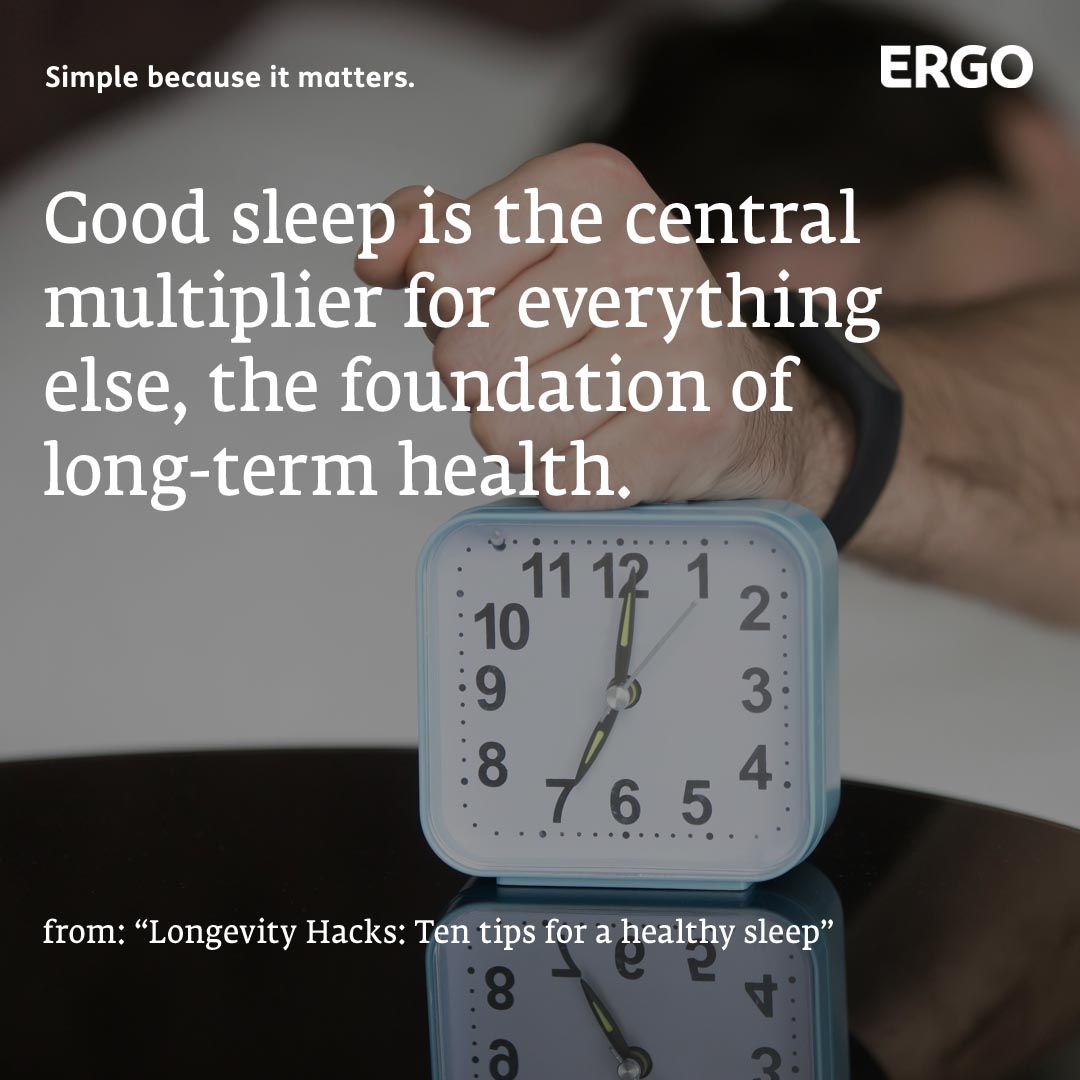 A male fist hits a light blue alarm clock on a table next to a bed.