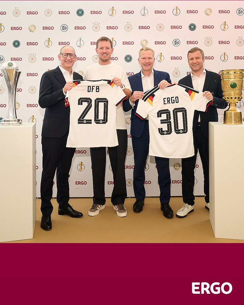 Four men are holding up two football shirts to the camera...