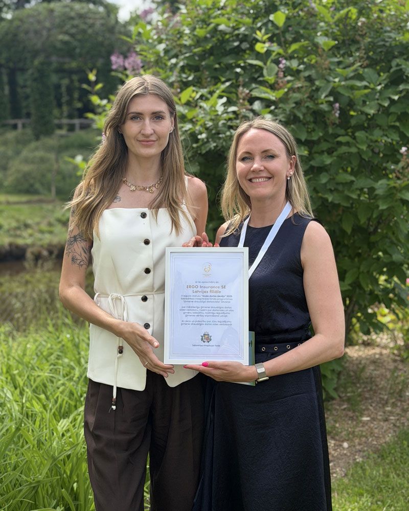 Two young women are standing outside in the countryside, holding a certificate up to the camera