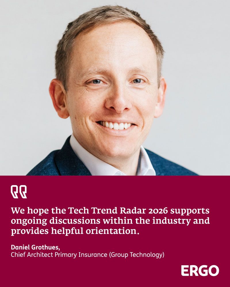 A young red-haired man in a blue suit smiles at the camera.