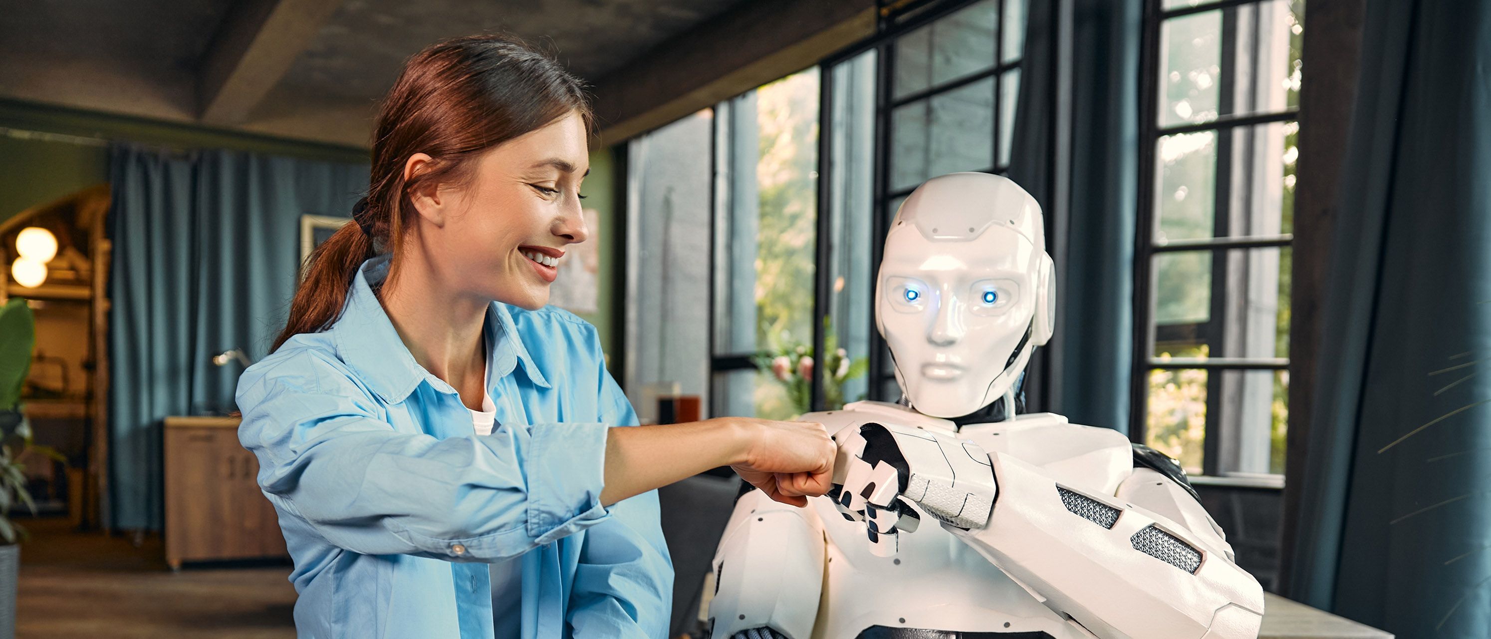 Einelachende Frau mit einem Robotor vor einem Laptop, die sich abklatschen.