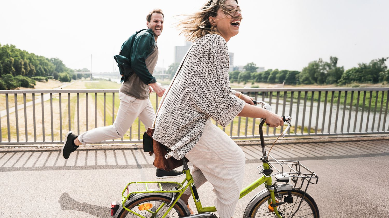 A smiling woman on a green bicycle next to a man in casual clothing jogging.